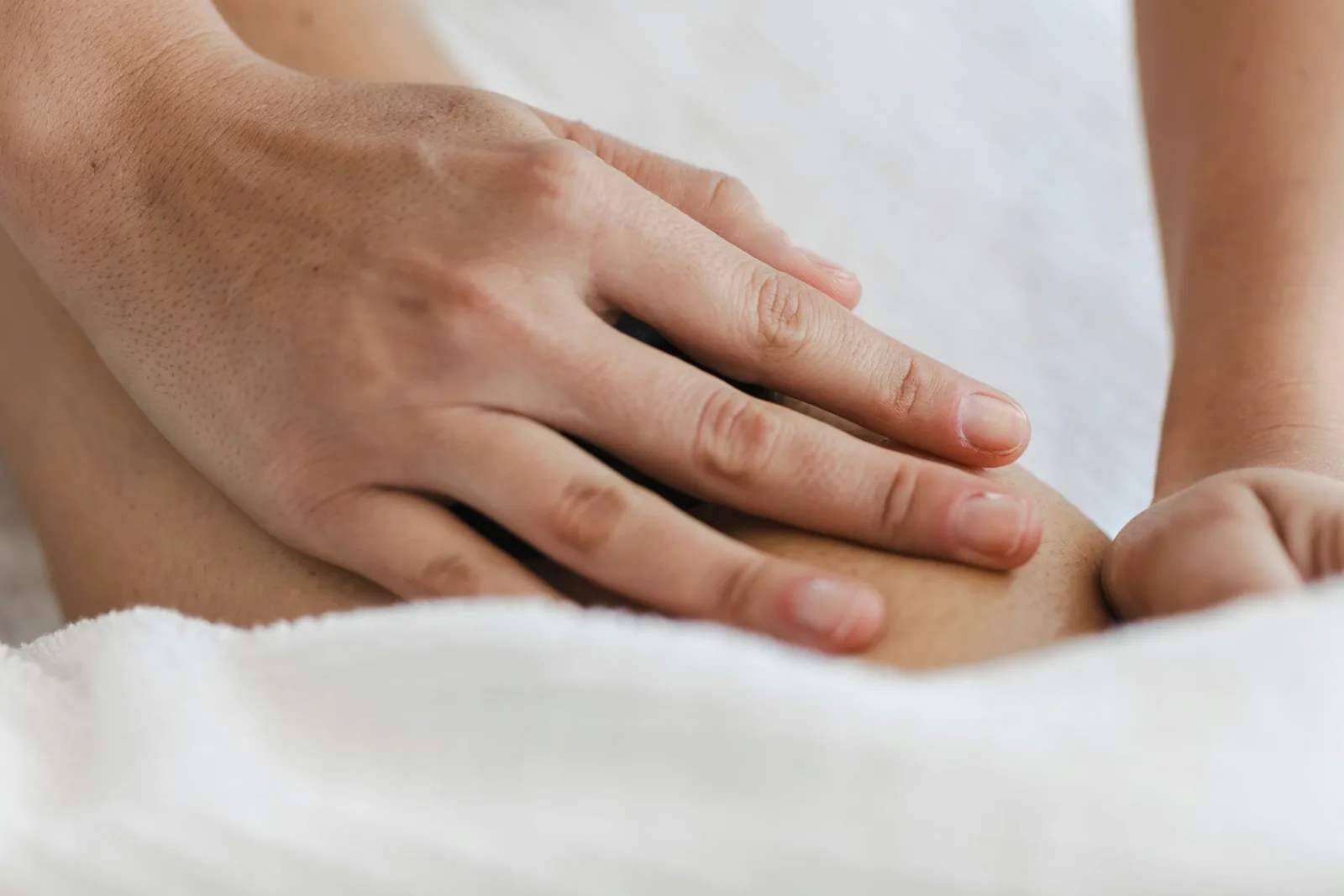 Therapist's hands resting lightly on a person's lower leg on a white towel