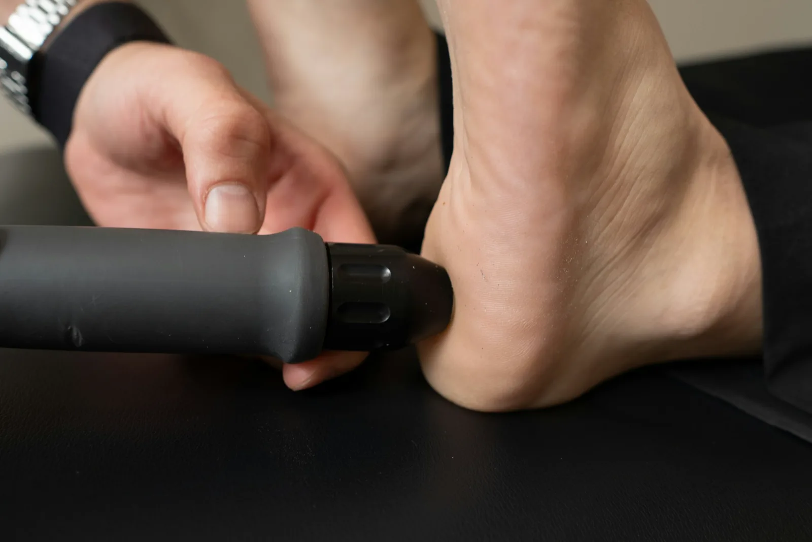 Handheld massage device pressed against the heel of a bare foot