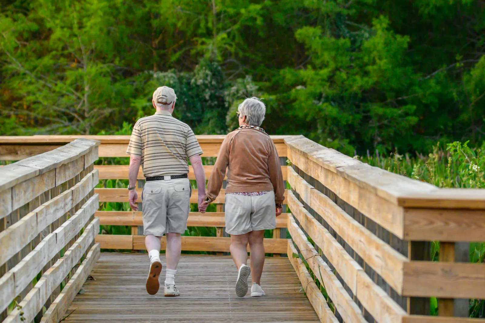 Older couple walking together across a wooden footbridge in a park